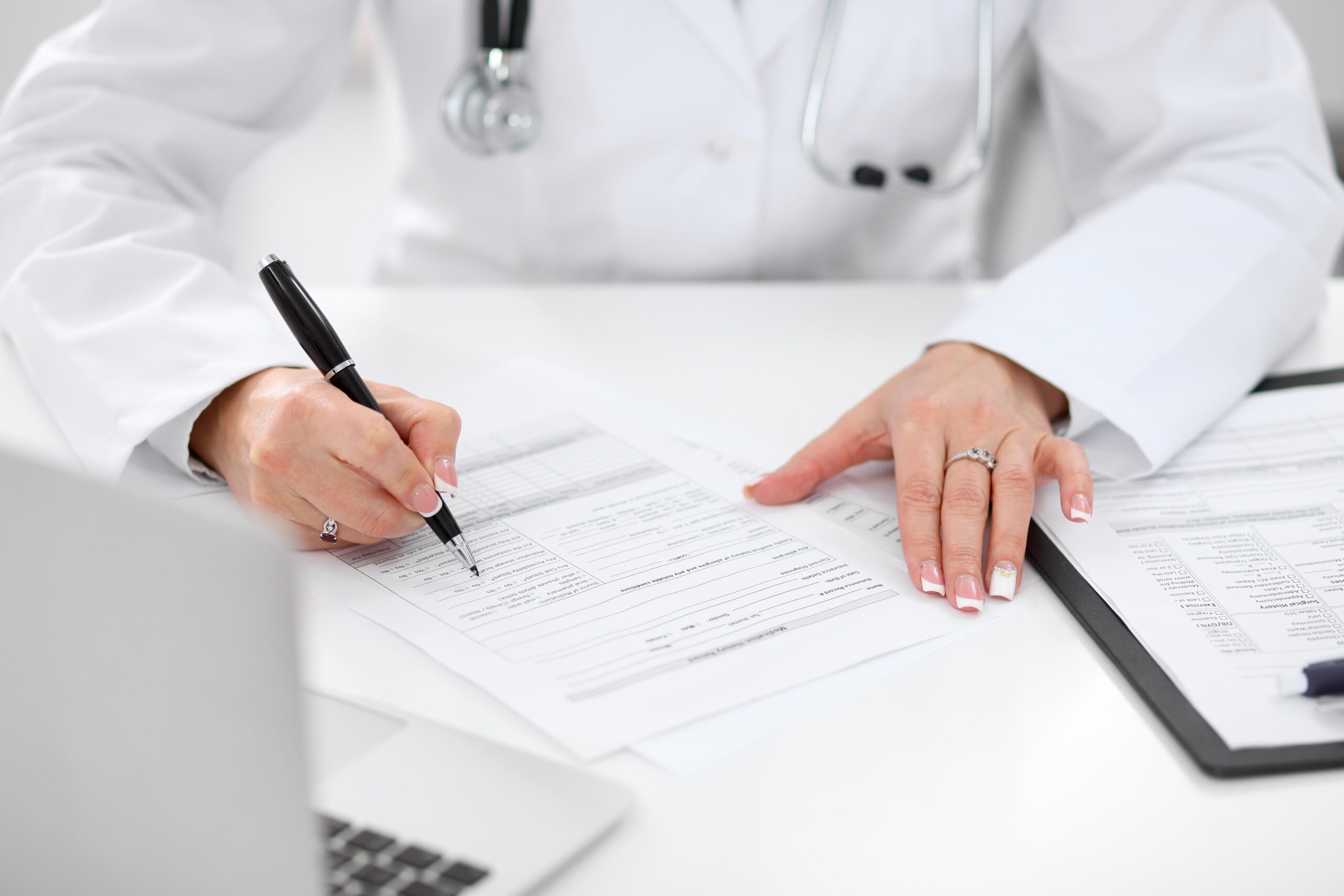 medical professional filling a medical information form next to an open laptop